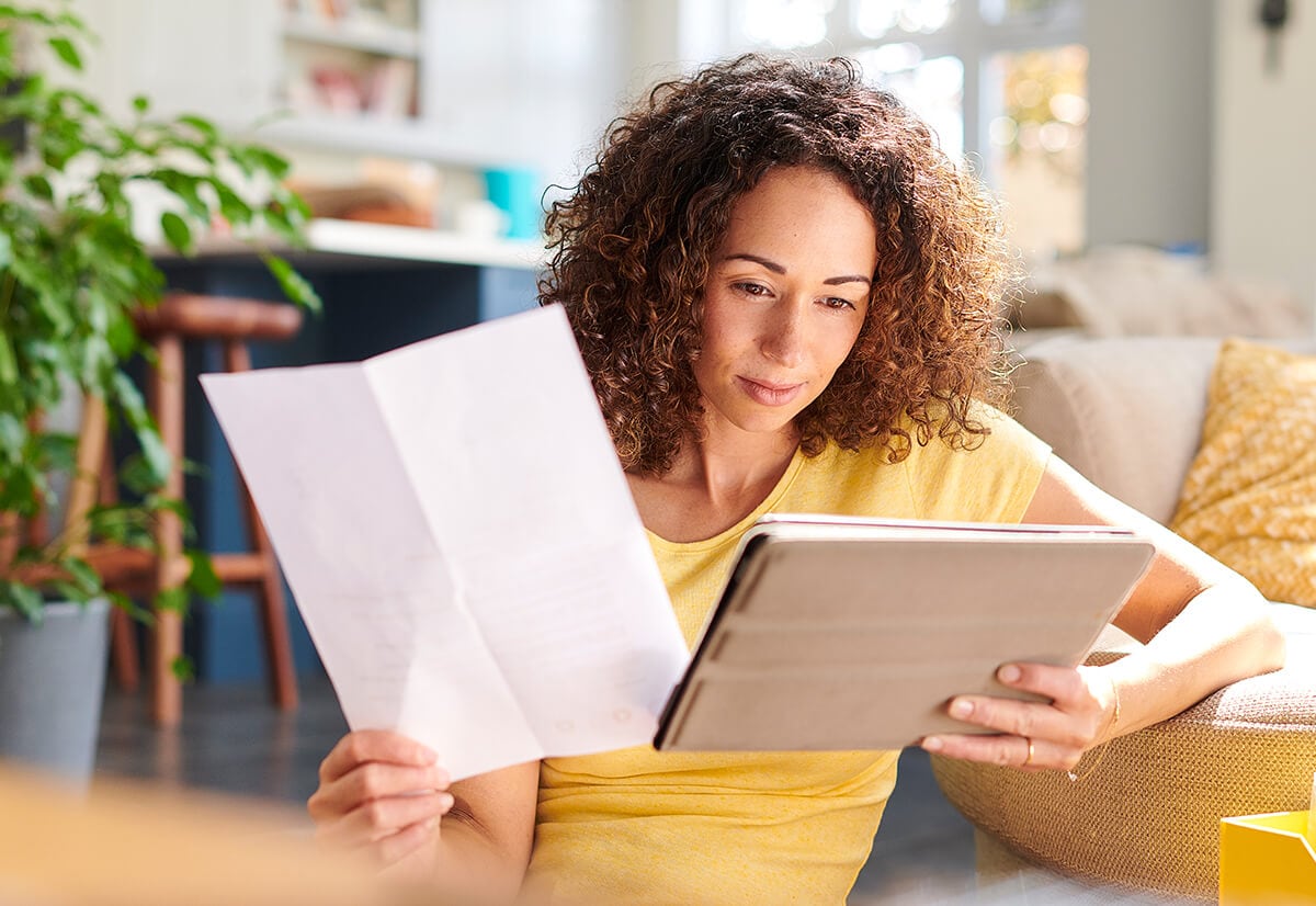 A woman sitting on the floor at home working on her tablet.