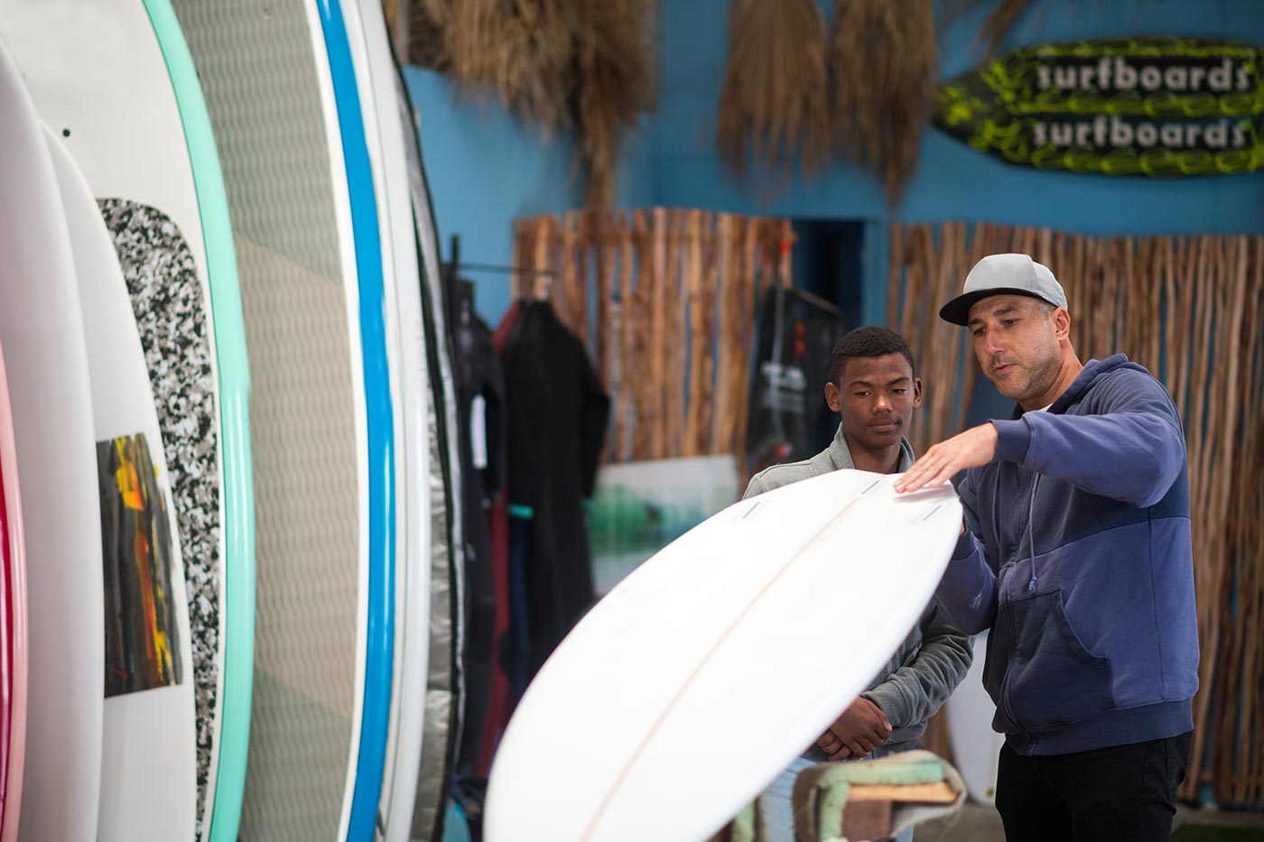 Two men in surf shop examining a surfboard.