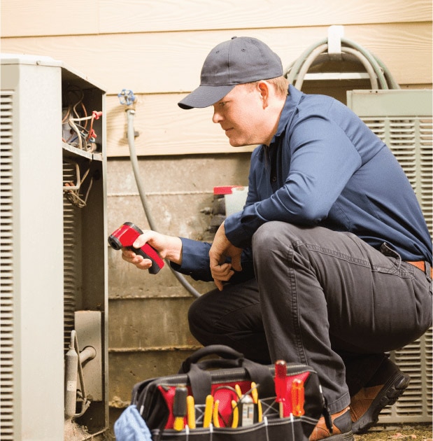 HVAC professional crouching next to heat pump.