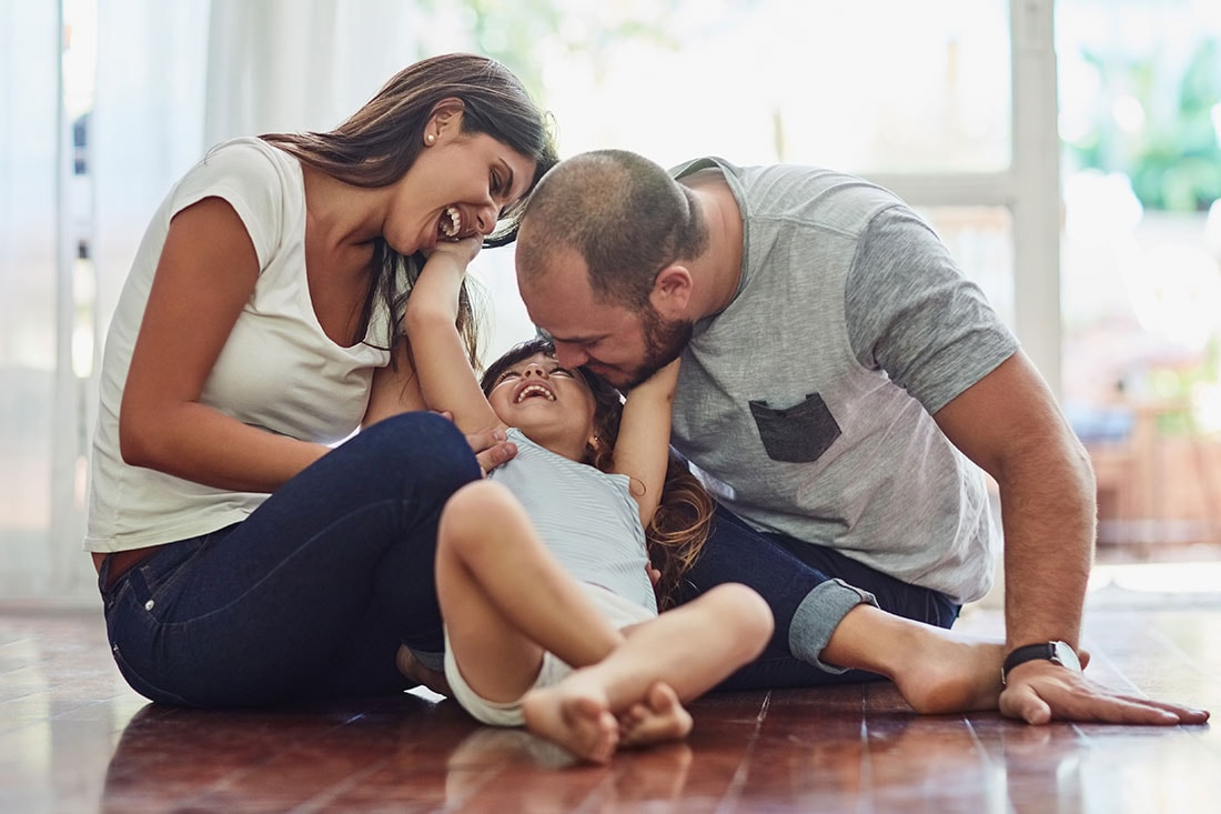 Husband and wife sitting on the living room floor playing with daughter.