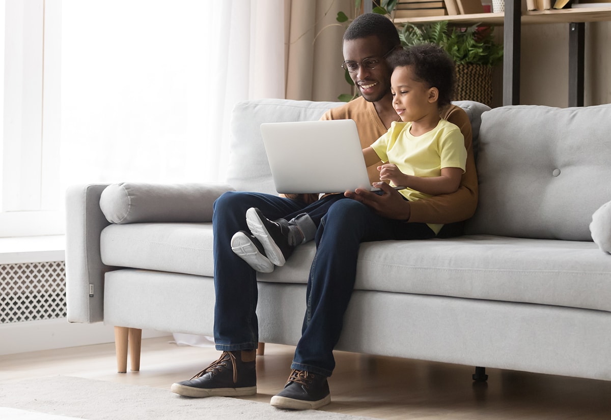 A young man and his son using a laptop together in their living room